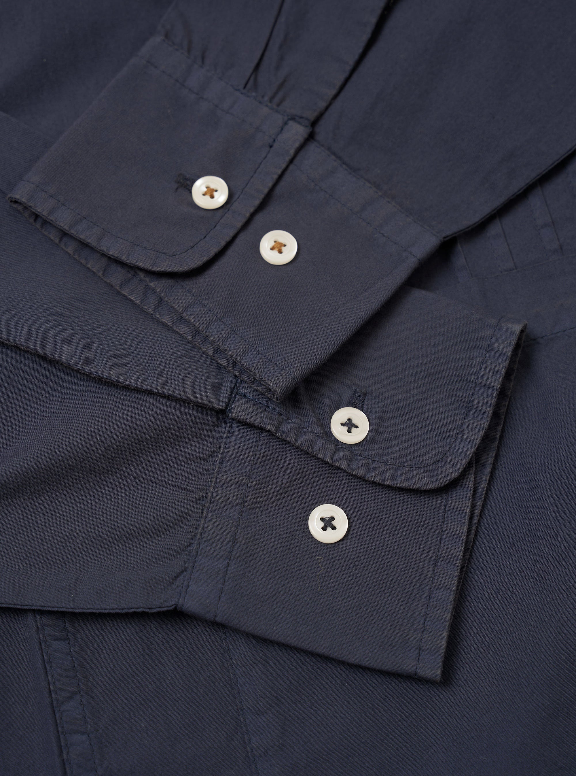 The Navy Poplin Dwight Overshirt is shown in a detail view as a flat lay against a white background. The image focuses on the lower front corner of the garment, highlighting a large patch pocket with a button-down flap and the clean, lightweight texture of the navy blue cotton poplin fabric.