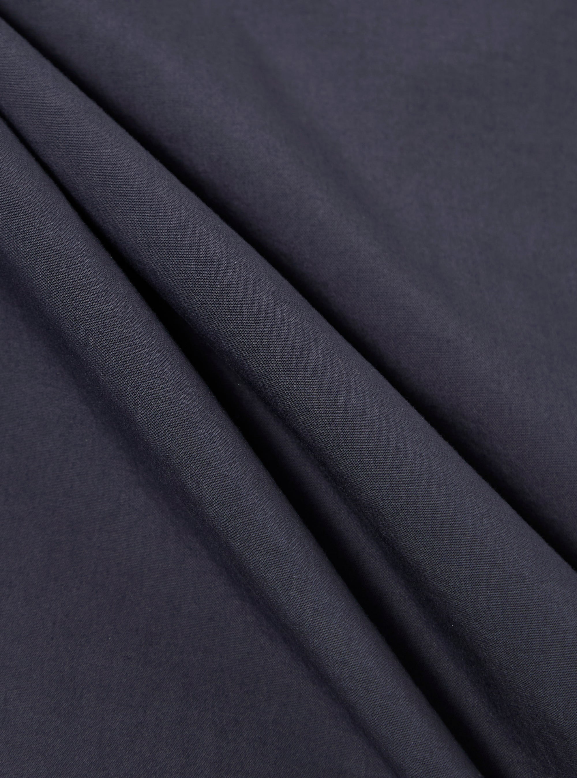 A close-up fabric swatch of the Navy Poplin Dwight Overshirt displays a deep navy blue color with a smooth, tight poplin weave. The image focuses entirely on the textile's surface and color.