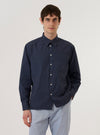 A model wears the Navy Poplin Patched Lazy Day Shirt while standing against a plain white background. The shirt features a button-down front, a classic collar, and tonal navy patches on the chest and body. The model is shown from the waist up, with the shirt worn over a white T-shirt.