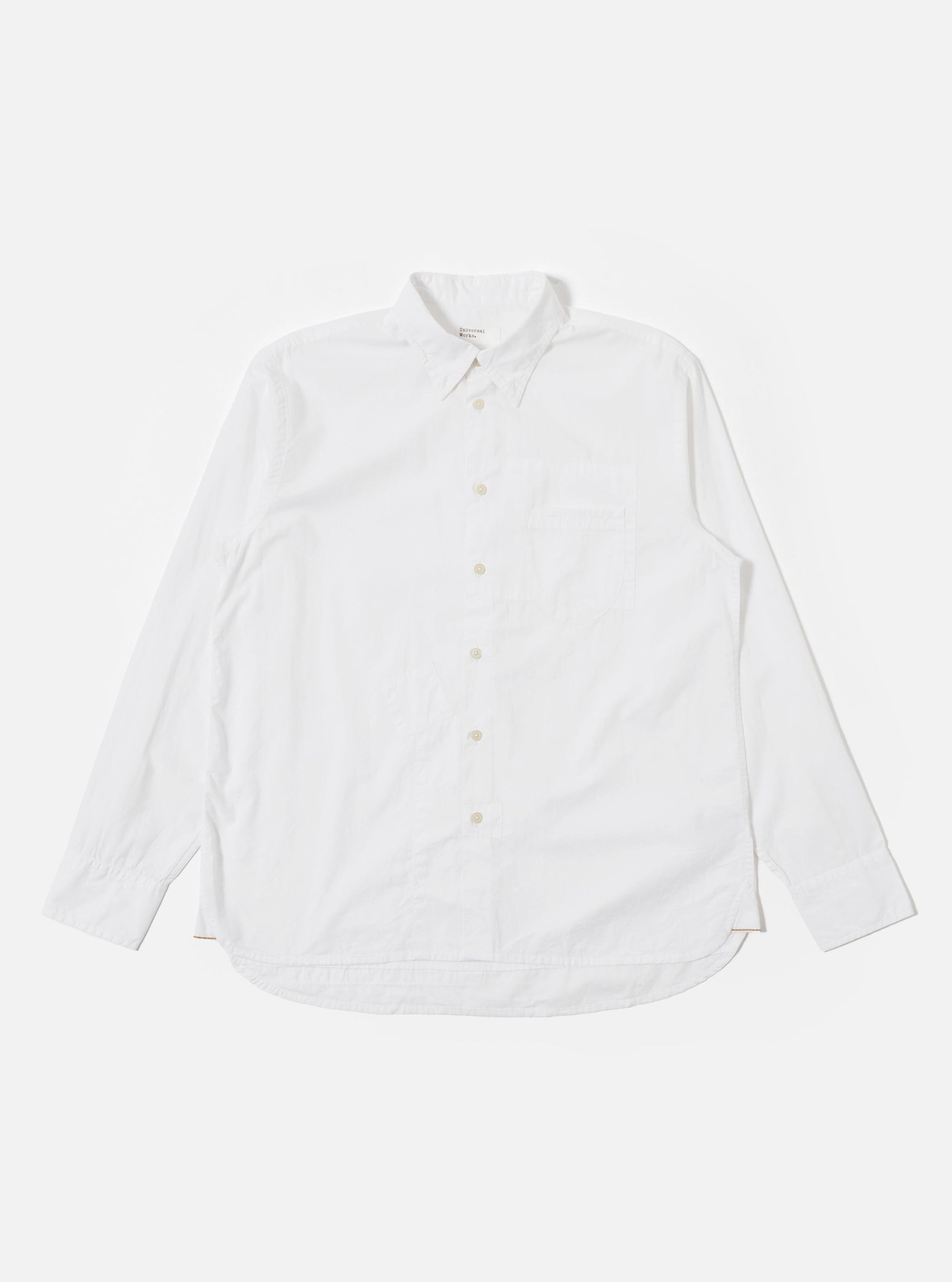 The White Poplin Patched Lazy Day Shirt is shown as a flat lay against a plain white background. The shirt features a relaxed fit, a simple pointed collar, and a central button-down front. A prominent design element is the single asymmetric chest pocket. The fabric is a crisp, solid white cotton poplin.