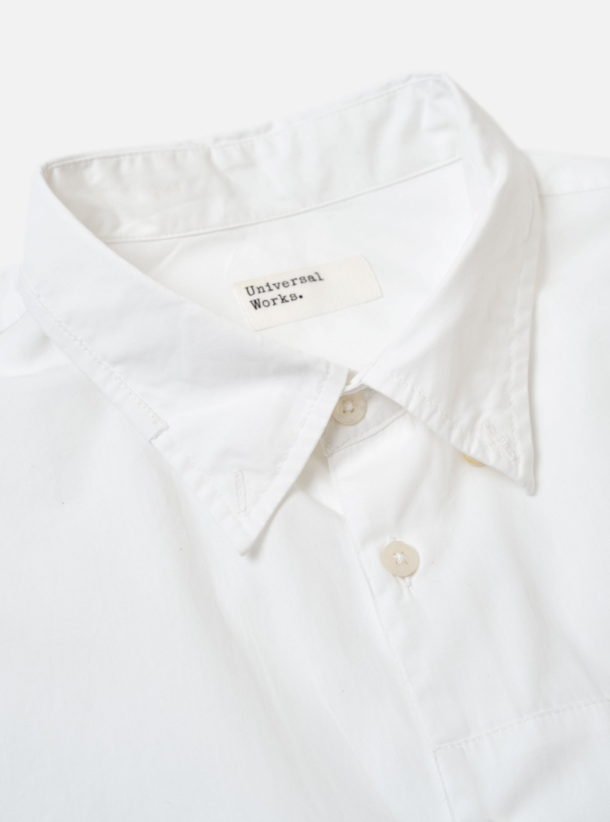 The White Poplin Patched Lazy Day Shirt is shown as a flat lay against a white background. The shirt features a classic pointed collar, a full button-down front, and two large patch pockets at the chest and hip. The fabric is a smooth cotton poplin in an off-white ecru shade.