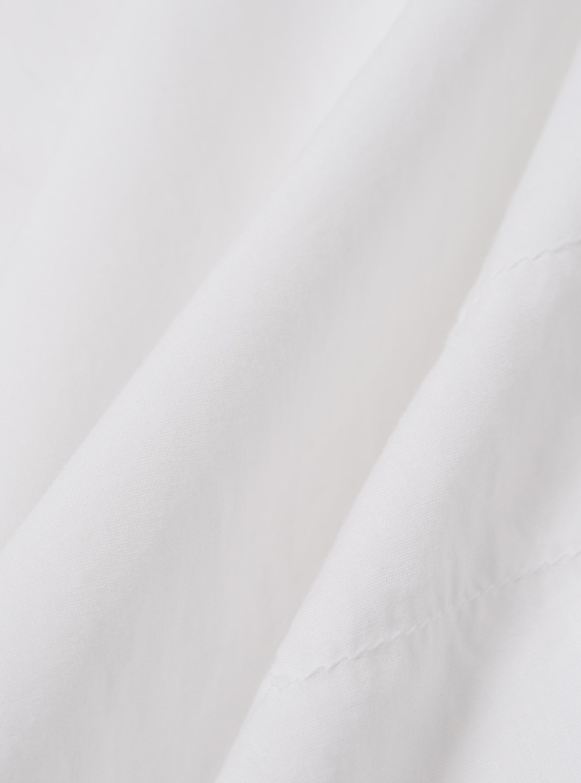 A close-up fabric swatch of the White Poplin Patched Lazy Day Shirt highlights the smooth, fine weave of the ecru cotton poplin material. The image focuses on the textile detail and color. No model or mannequin is present.