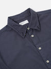 The Navy Poplin Patched Lazy Day Shirt is shown from a rear angle as a flat lay against a plain white background. The image highlights the smooth navy blue poplin fabric, a simple straight hem, and a clean back yoke with a central box pleat.