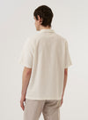 A model wears the Ecru Dot Waffle Road Shirt, featuring a camp collar, short sleeves, and a textured dot waffle fabric. The model is photographed from the waist up against a plain light gray background. The shirt is shown partially unbuttoned over a white t-shirt.