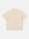 The Ecru Dot Waffle Road Shirt is shown as a flat lay against a white background. The short-sleeve shirt features a camp collar with a loop closure, a central button-down front, and a single patch pocket on the left chest. The ecru-colored cotton fabric has a distinct dot waffle texture and a straight hem.