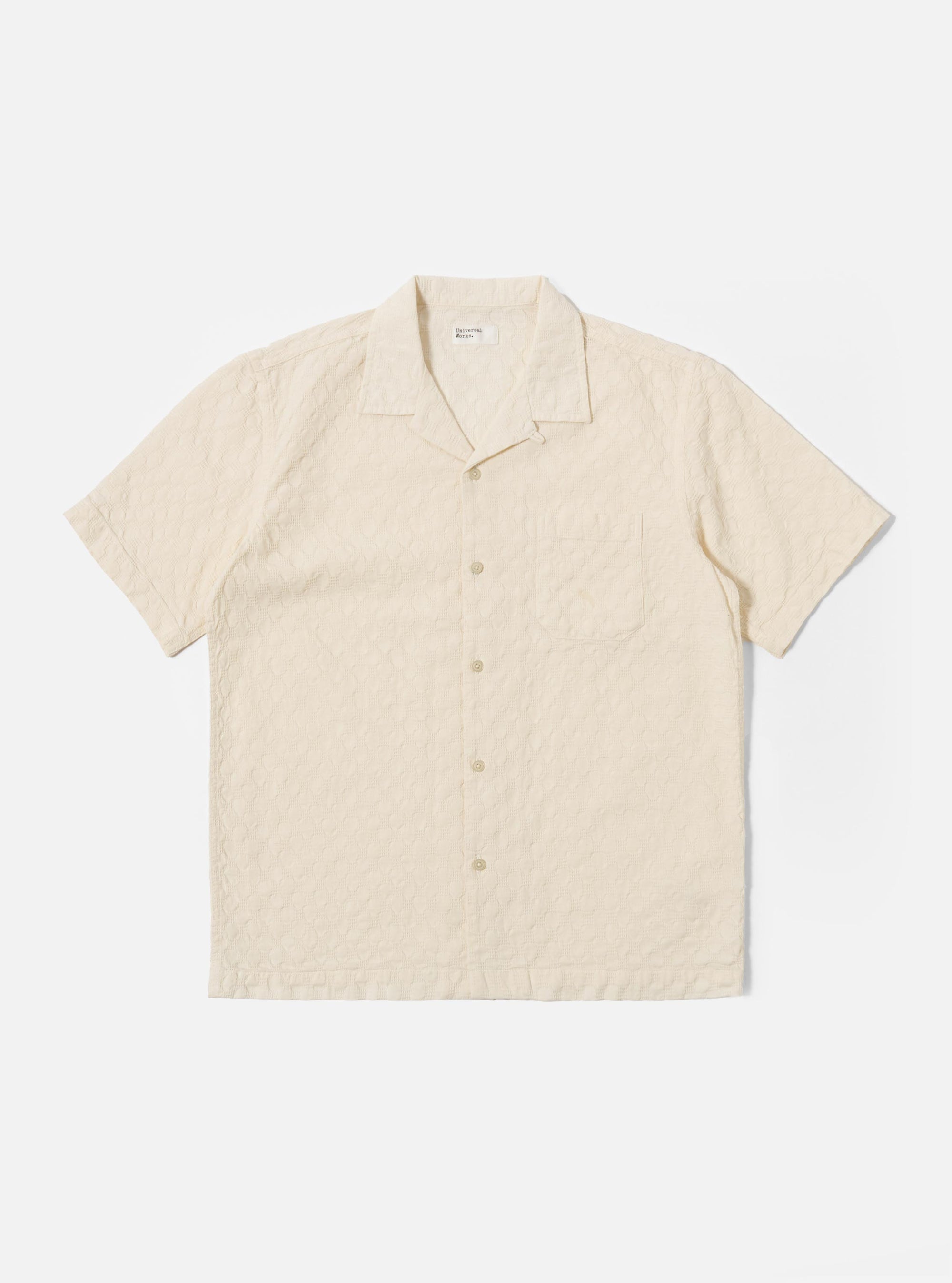 The Ecru Dot Waffle Road Shirt is shown as a flat lay against a white background. The short-sleeve shirt features a camp collar with a loop closure, a central button-down front, and a single patch pocket on the left chest. The ecru-colored cotton fabric has a distinct dot waffle texture and a straight hem.