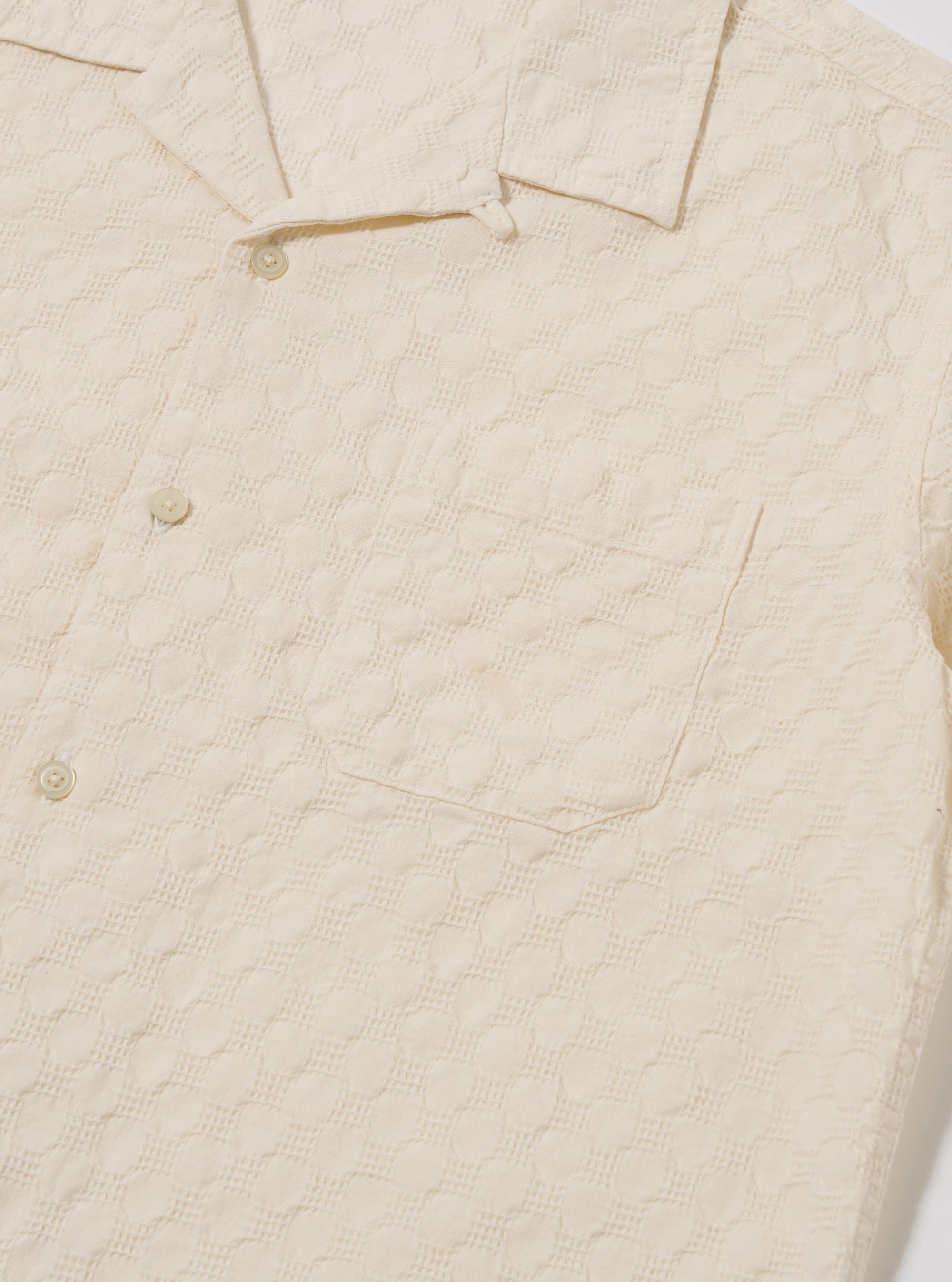 The Ecru Dot Waffle Road Shirt is shown from the back as a flat lay against a plain white background. The image highlights the shirt's straight hem, short sleeves, and the unique textured dot waffle pattern of the ecru cotton fabric.
