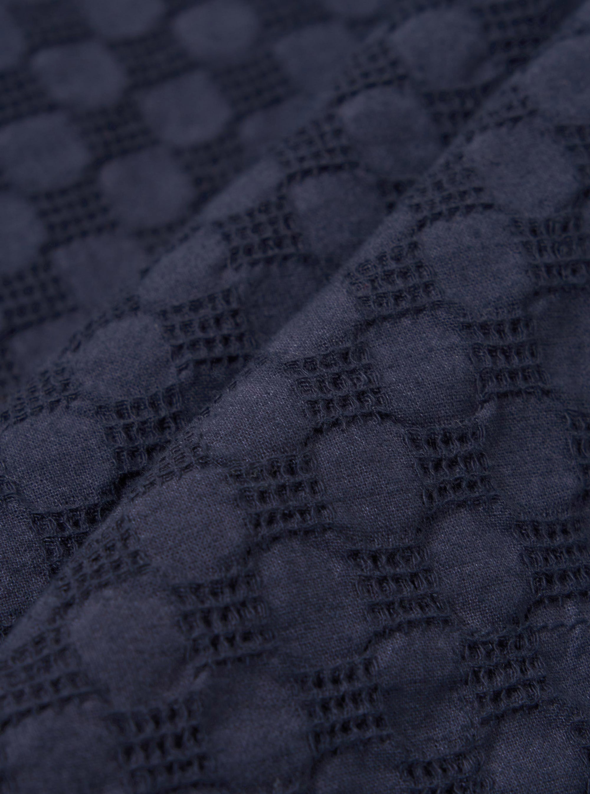 A close-up fabric swatch of the Navy Dot Waffle Road Shirt is shown, highlighting the deep navy blue color and the intricate waffle-weave texture with a subtle dot pattern. The textured cotton fabric fills the frame.