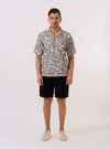 The Ecru/Black Kantha Flower Road Shirt is shown as a flat lay against a plain white background. The shirt features a camp collar, a full-length button front, and a single chest pocket on the left side. The fabric has an all-over intricate black floral pattern on an ecru base, characteristic of the Kantha Flower design.