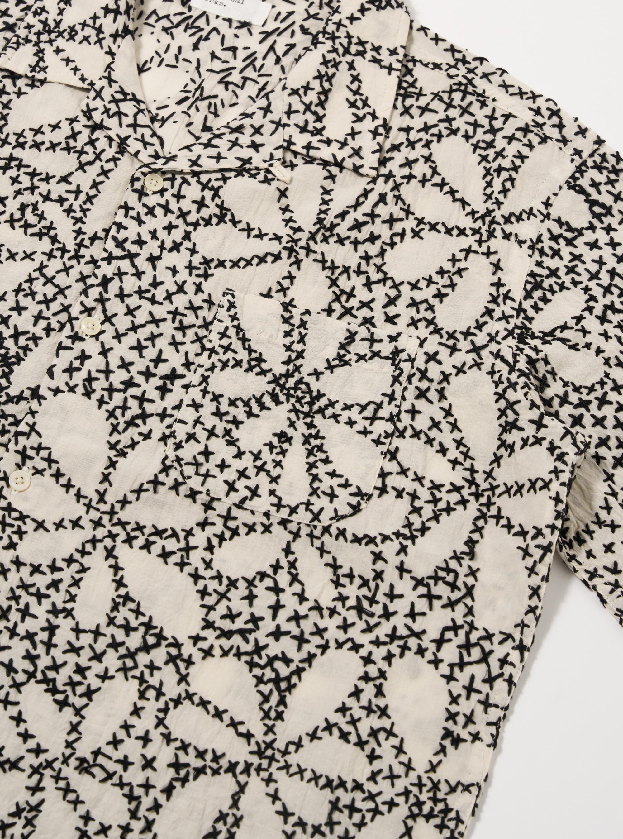 The Ecru/Black Kantha Flower Road Shirt is shown from the back as a flat lay against a plain white background. The short-sleeve shirt features a straight hem and highlights the intricate black floral Kantha embroidery across the ecru cotton fabric.