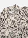 The Ecru/Black Kantha Flower Road Shirt is shown from a rear angle as a flat lay against a plain white background. The shirt features a straight hem and short sleeves, showcasing the intricate black floral Kantha embroidery across the ecru cotton fabric.