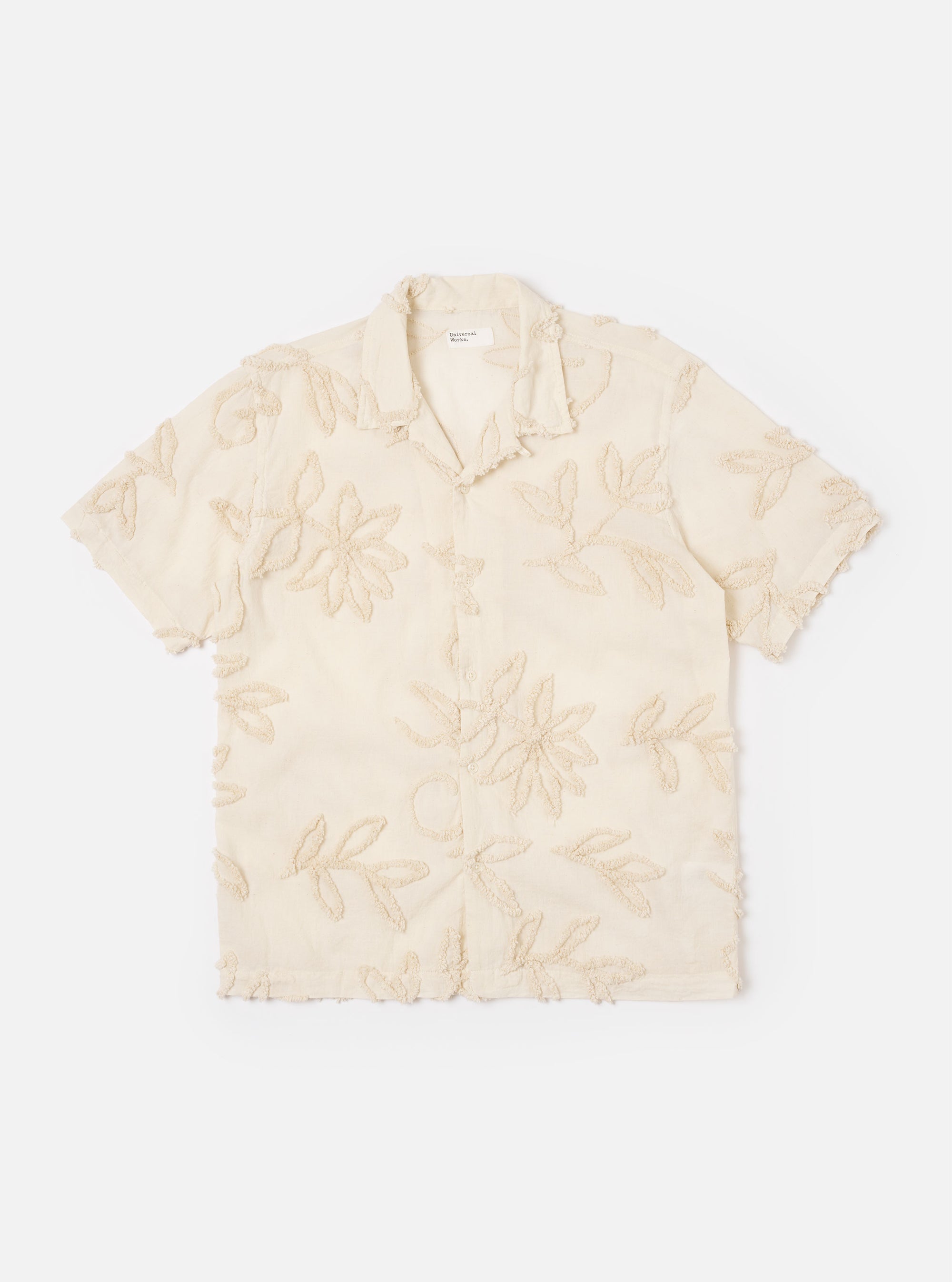 The Ecru 3D Flower Road Shirt is shown as a flat lay against a white background. The short-sleeve shirt features a single-piece loop-close collar, a straight hem, and a single chest patch pocket on the left side. The fabric is decorated with a tonal 3D flower pattern.