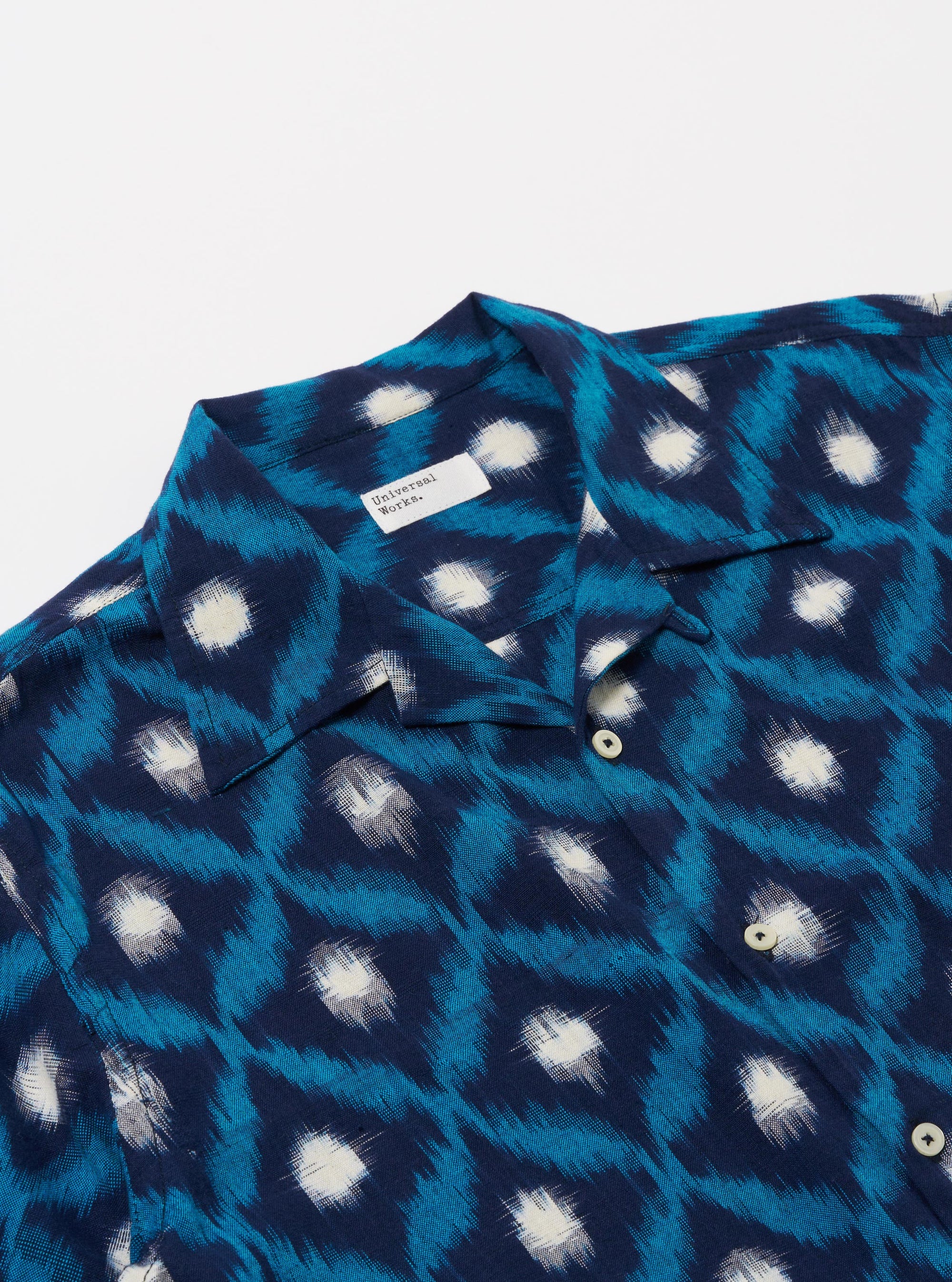 The Indigo Diamond Ikat Deck Shirt is shown from the back as a flat lay against a plain white background. The shirt features a dark indigo base with a repeating white diamond ikat pattern throughout. It has short sleeves and a straight hem.