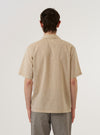 A model wears the Beige Fine Organic Cotton Sal Road Shirt, shown from the back against a plain white background. The shirt features a relaxed fit, short sleeves, and a straight hem. The light beige fabric is made from fine organic cotton and has a smooth appearance.