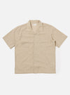The Beige Fine Organic Cotton Sal Road Shirt is shown as a flat lay against a white background. The short-sleeve shirt features a single-piece camp collar with a loop closure at the top, a straight hem, and two symmetrical patch pockets on the chest. The organic cotton fabric has a soft marled beige texture.