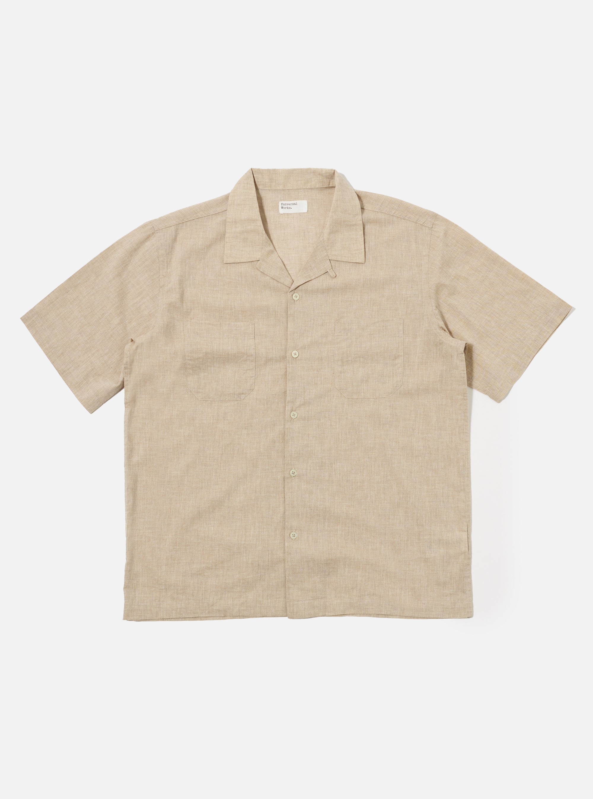 The Beige Fine Organic Cotton Sal Road Shirt is shown as a flat lay against a white background. The short-sleeve shirt features a single-piece camp collar with a loop closure at the top, a straight hem, and two symmetrical patch pockets on the chest. The organic cotton fabric has a soft marled beige texture.