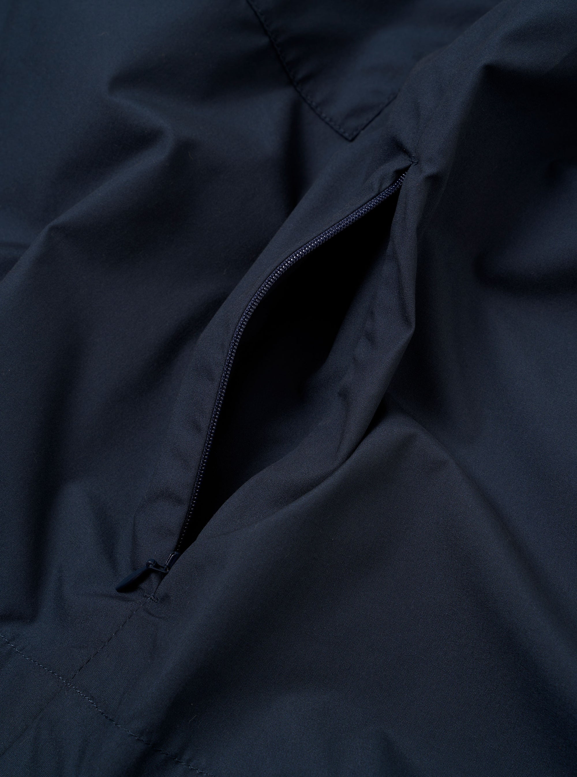 The Navy Recycled Polytech Z Tech Overshirt is shown as a flat lay against a plain white background. The image provides a detailed view of the short-sleeve overshirt, highlighting the smooth technical fabric and the reinforced patch chest pocket with its prominent vertical zipper. The garment features a simple one-piece collar and a full-length button placket.