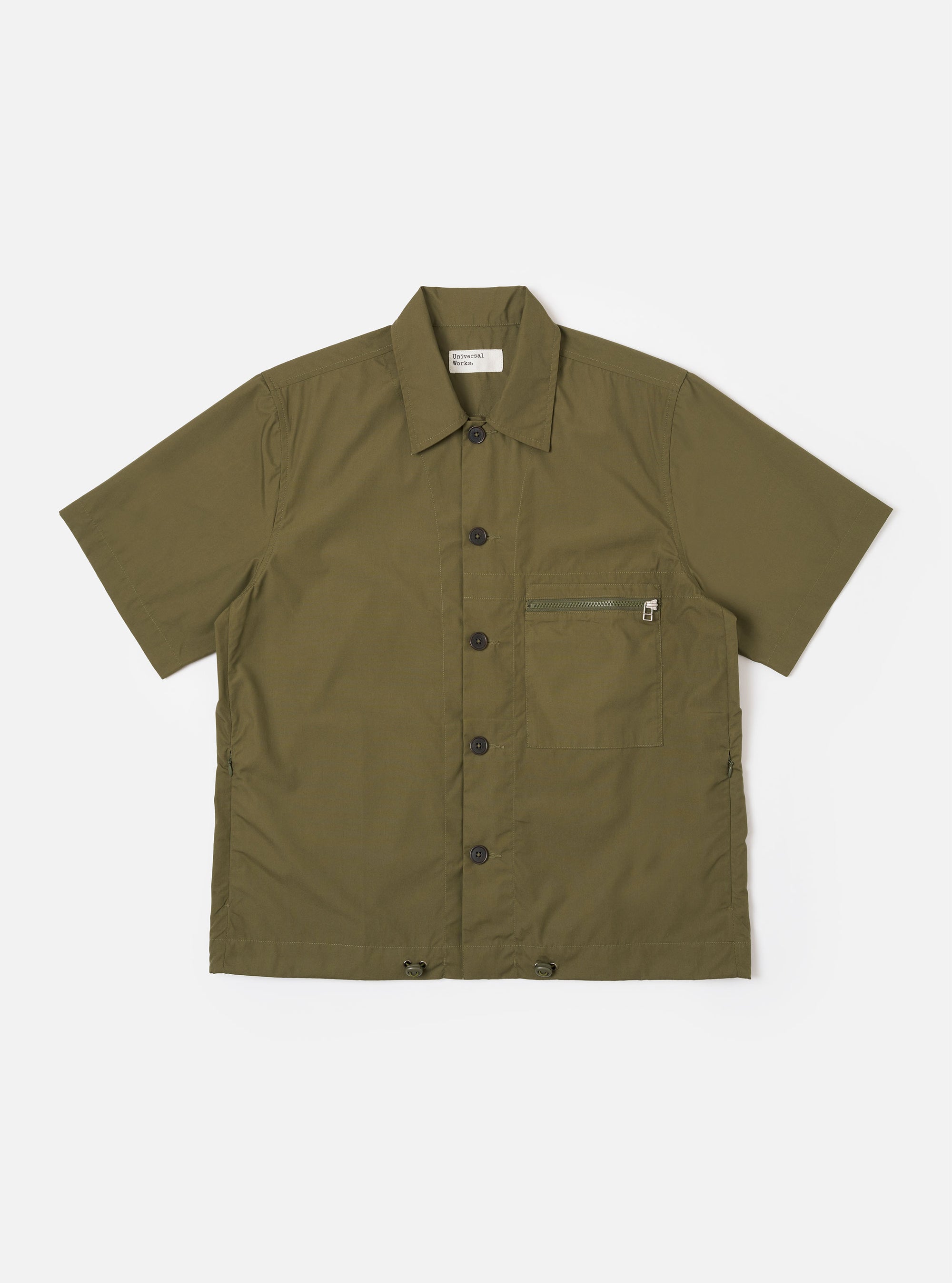 The Olive Recycled Polytech Z Tech Overshirt is shown as a flat lay against a white background. The short-sleeve overshirt features a one-piece collar, a central button-down front, and a single reinforced patch pocket with a zip on the chest. The olive green fabric has a smooth finish and visible stitching details.