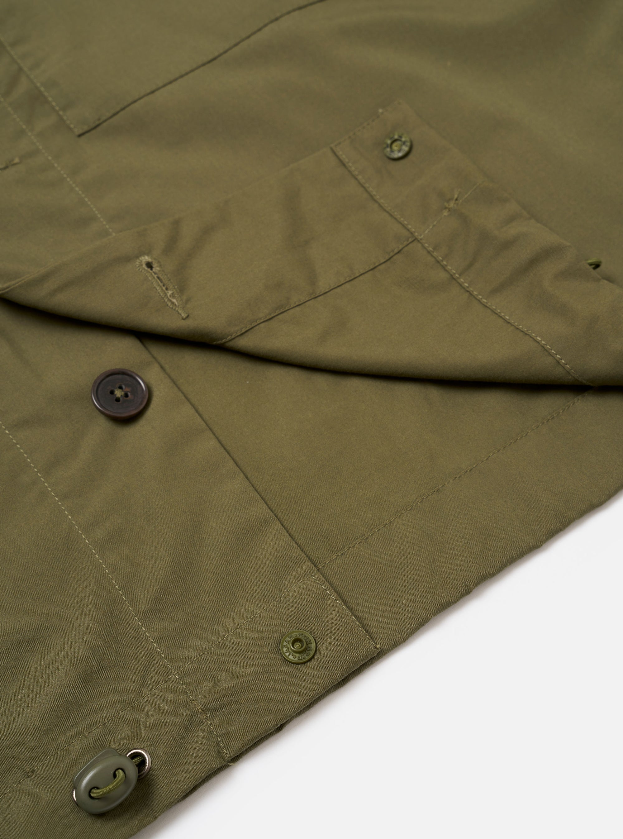 The Olive Recycled Polytech Z Tech Overshirt is shown in a detail view as a flat lay against a plain white background. The image focuses on the lower portion of the garment, highlighting the smooth olive green recycled polytech fabric, the straight hemline, and the clean stitching of the side seam.