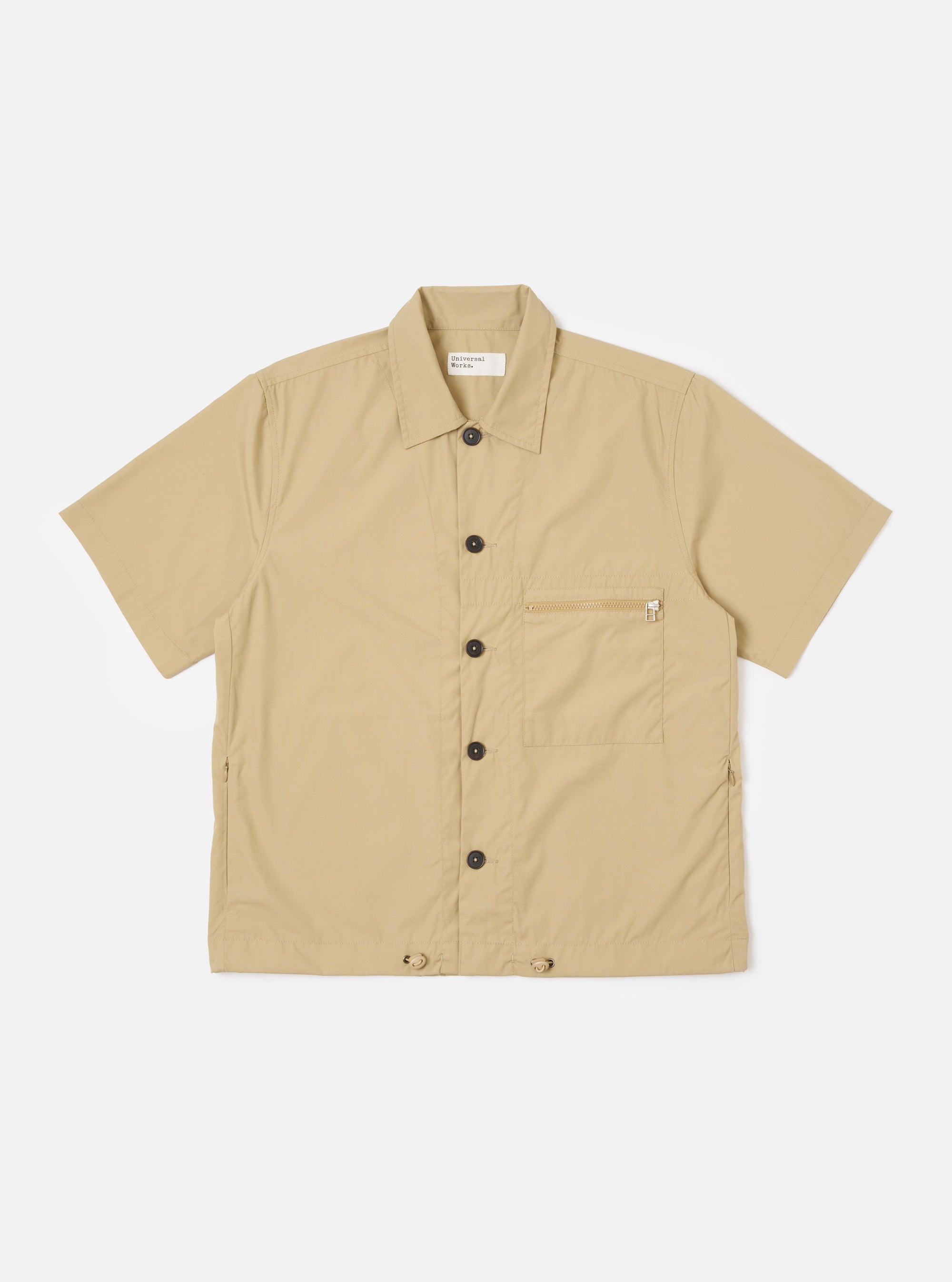 The Sand Recycled Polytech Z Tech Overshirt is shown as a flat lay against a white background. The overshirt features a one-piece collar, a central front closure, and a single reinforced vertical zip pocket on the left chest. The sand-colored fabric has a smooth, technical finish, and the garment is designed with a boxy fit and a straight hem.