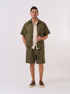 The Olive Recycled Polytech Z Tech Overshirt is shown as a flat lay against a plain white background. The overshirt features a one-piece collar, a central button-down front, and a single reinforced patch pocket on the chest with a vertical zip closure. The olive green fabric has a smooth, technical finish, and the garment is designed with a straight hem and adjustable elasticated drawcords.