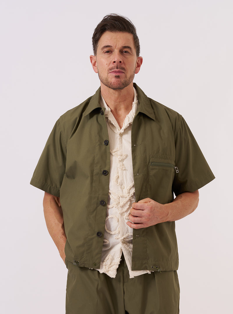 A model wears the Olive Recycled Polytech Z Tech Overshirt over a light-colored shirt, standing against a plain white background. The overshirt features a full-length front zipper, two large chest patch pockets, and a classic collar. The olive green fabric is smooth with a technical finish.