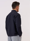 A model wears the Navy Seo Recycled Nylon Zip Too Shirt over a light-colored top, shown from a side-angle view against a plain, neutral studio background. The shirt features a smooth technical fabric made from recycled nylon, a pointed collar, and a full-length front zipper. The relaxed silhouette and deep navy color are prominent.
