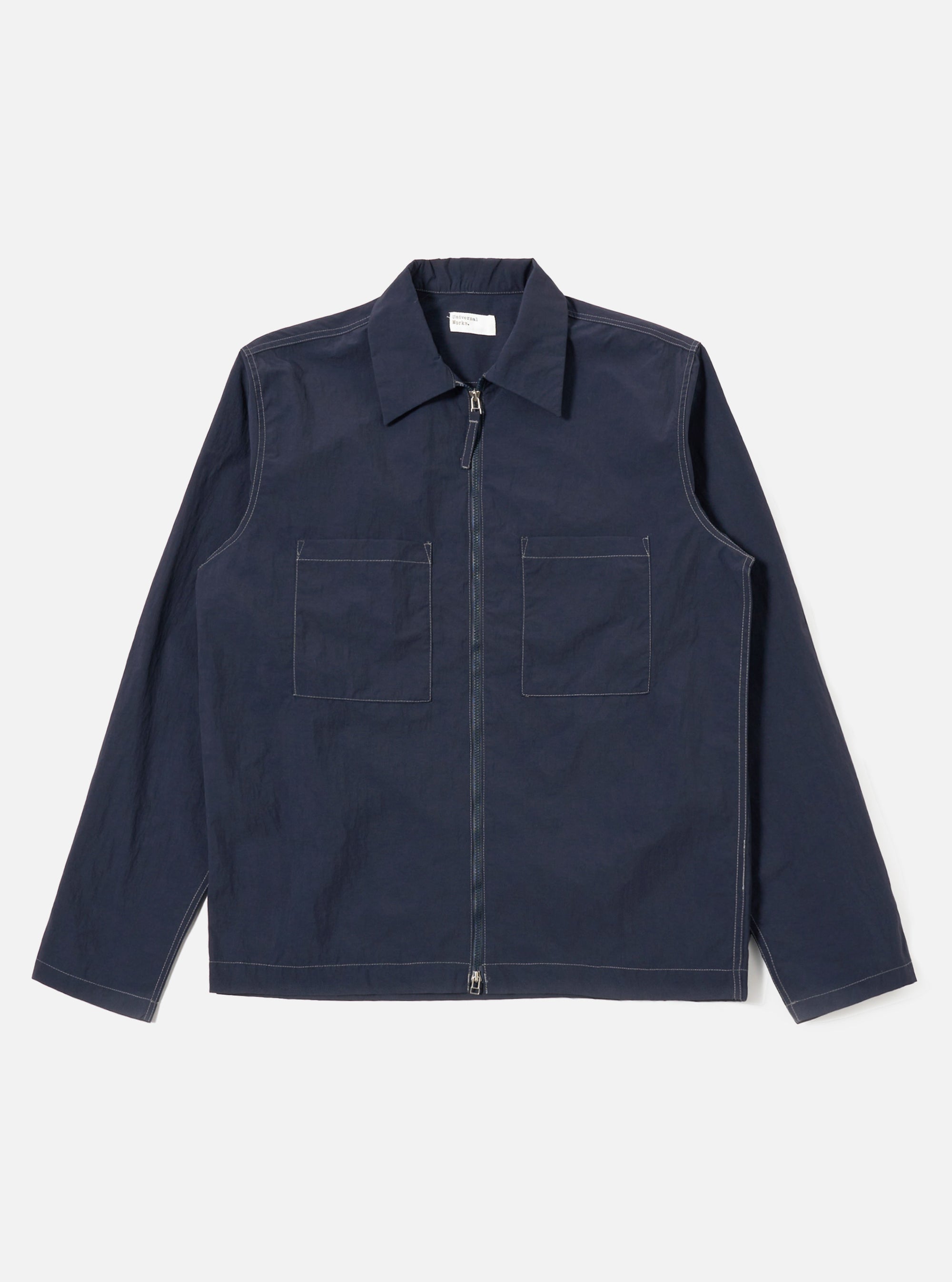 The Navy Seo Recycled Nylon Zip Too Shirt is shown as a flat lay against a white background. The shirt features a two-way front zip closure, a structured collar, and two large patch pockets at the chest. It has long sleeves with simple cuffs and a straight hem. The garment is made from a smooth, dark navy recycled nylon fabric.