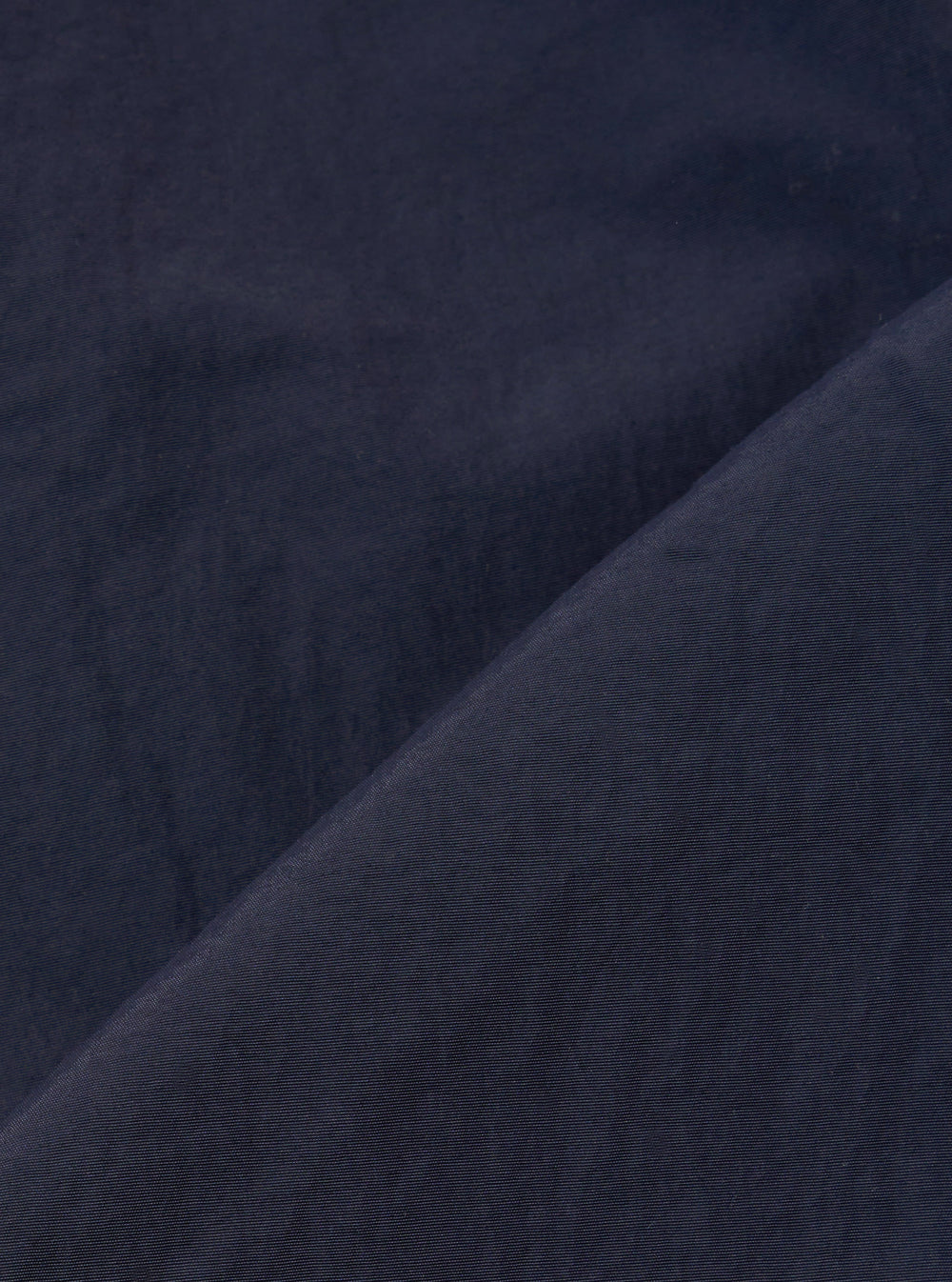 A close-up fabric swatch of the Navy Seo Recycled Nylon Zip Too Shirt highlights the smooth, technical texture of the recycled nylon material. The fabric is a solid, deep navy blue with a slight matte finish and a visible fine-grained weave.