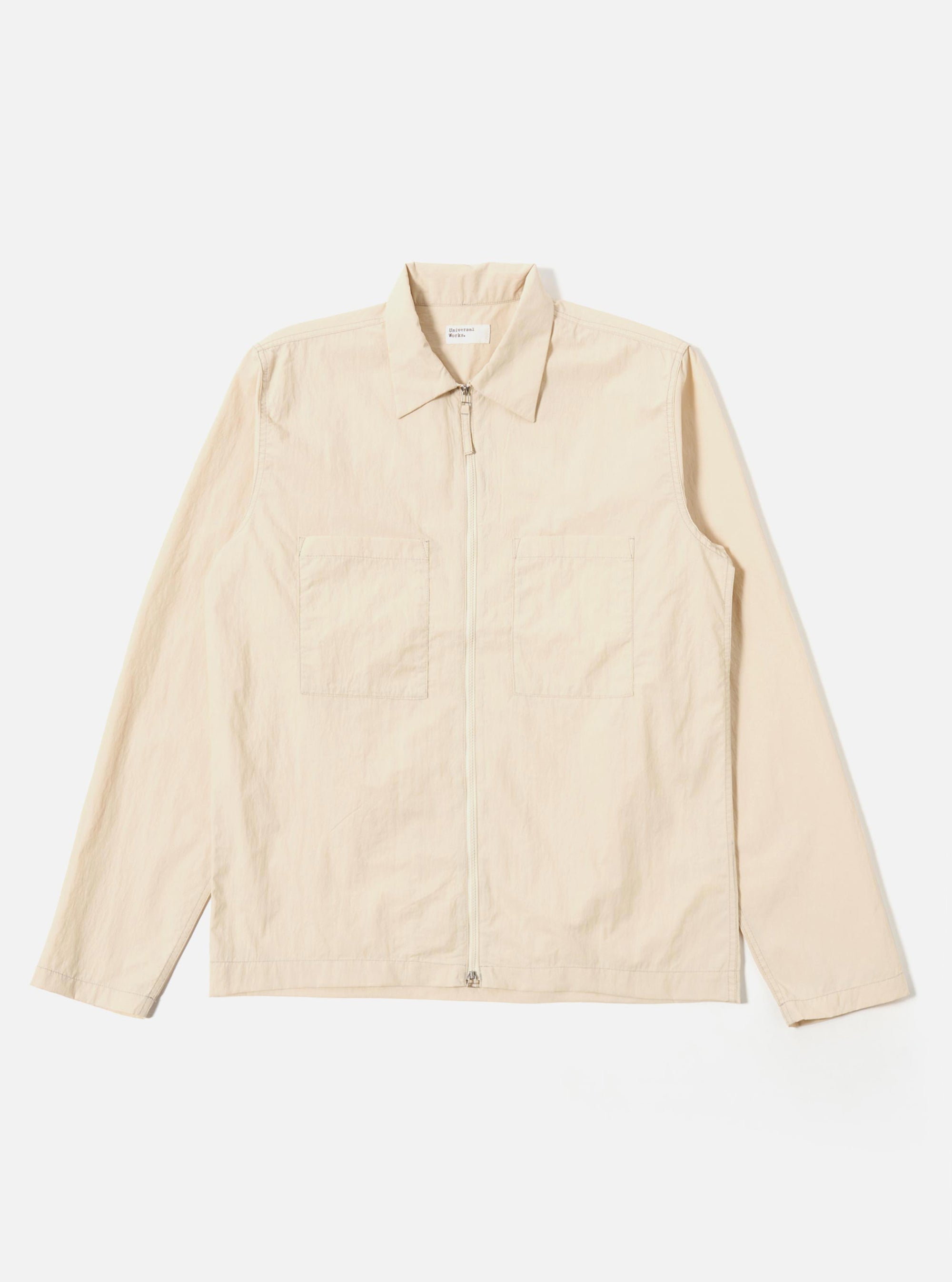 The Stone Seo Recycled Nylon Zip Too Shirt is shown as a flat lay against a plain white background. The shirt features a full-length central zip closure, a classic pointed collar, and two large patch pockets at the waist. The garment is made from a smooth, stone-colored recycled nylon fabric with visible tonal stitching.