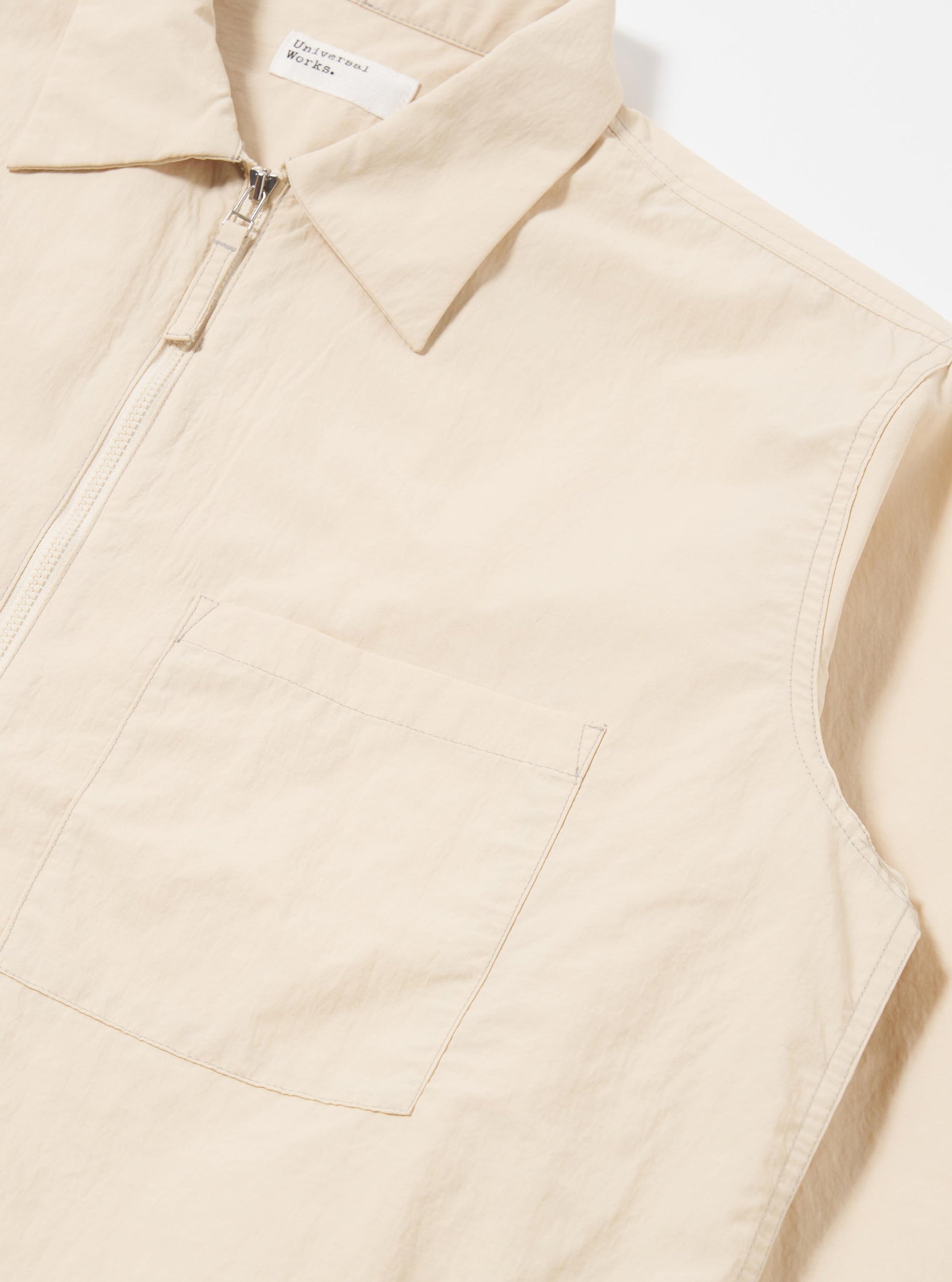 The Stone Seo Recycled Nylon Zip Too Shirt is shown in a detail view as a flat lay against a plain white background. The image highlights the smooth, technical texture of the stone-colored recycled nylon fabric and the construction of a chest patch pocket.