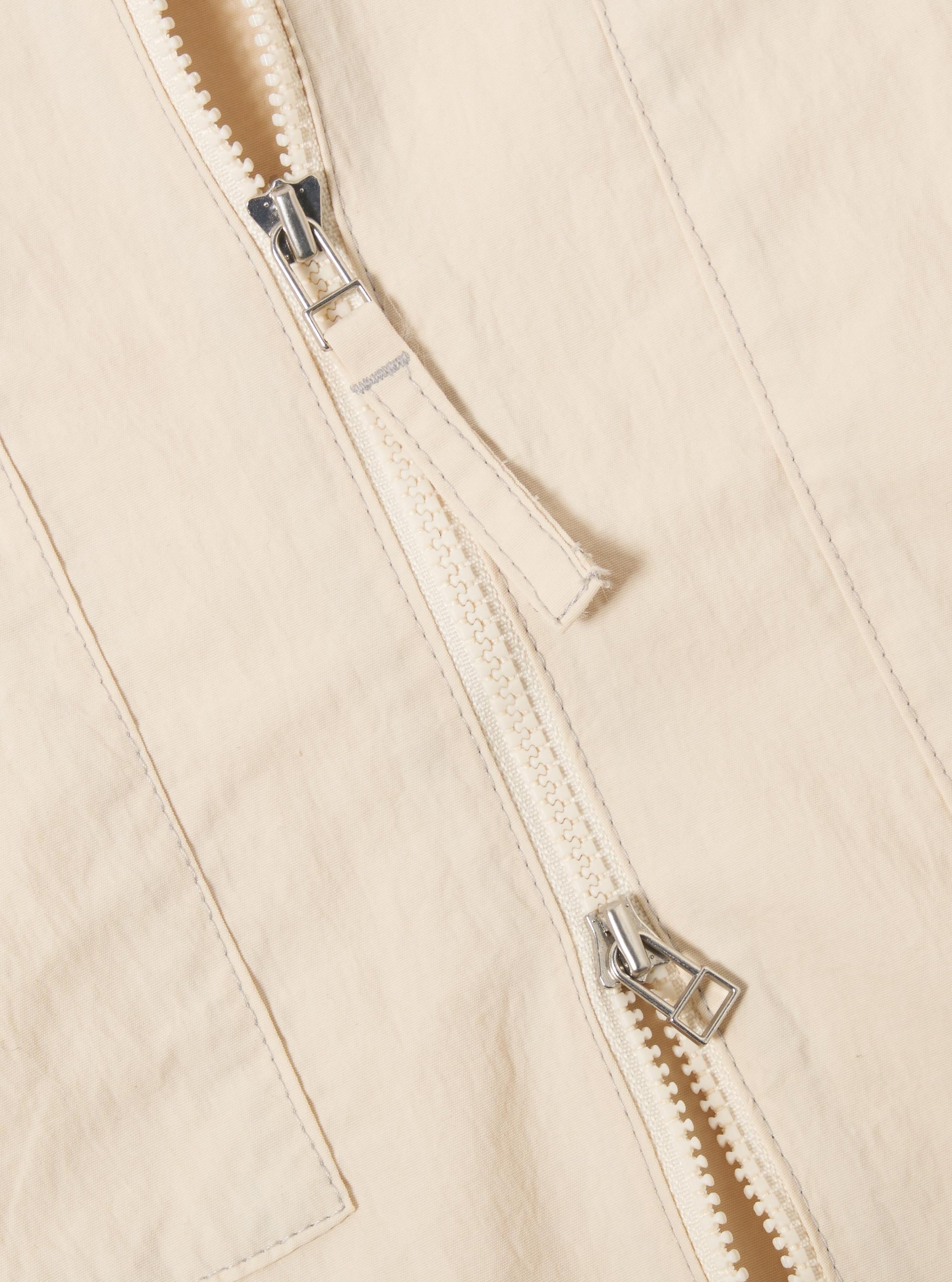 The Stone Seo Recycled Nylon Zip Too Shirt is shown in a detail view as a flat lay against a plain white background. The image highlights the smooth texture of the stone-colored recycled nylon fabric and the construction of the chest patch pocket with a visible horizontal seam.