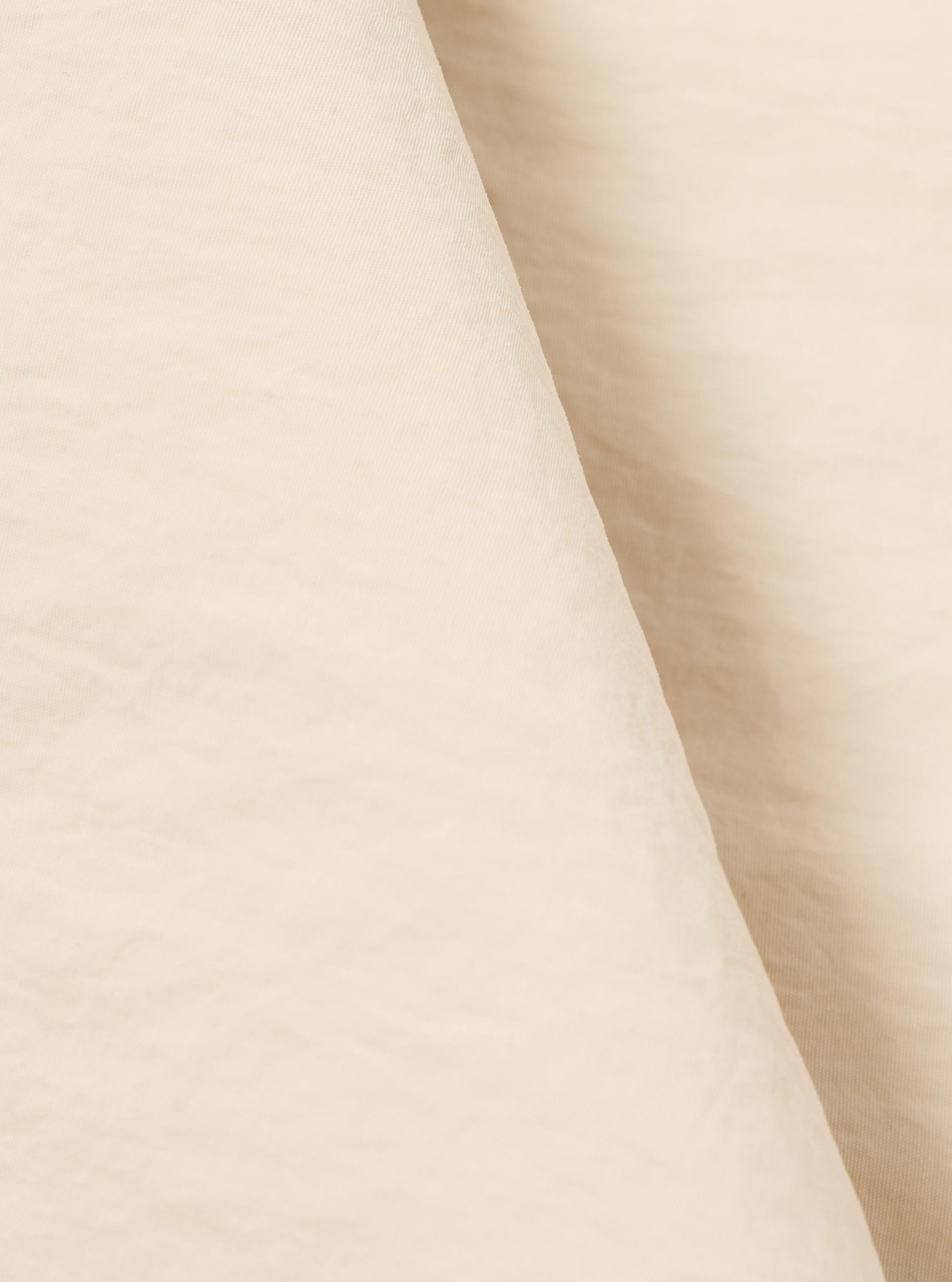 A close-up fabric swatch of the Stone Seo Recycled Nylon Zip Too Shirt highlights the light stone color and the smooth, technical texture of the recycled nylon material. The fabric fills the frame, providing a detailed view of the garment's weave and color.