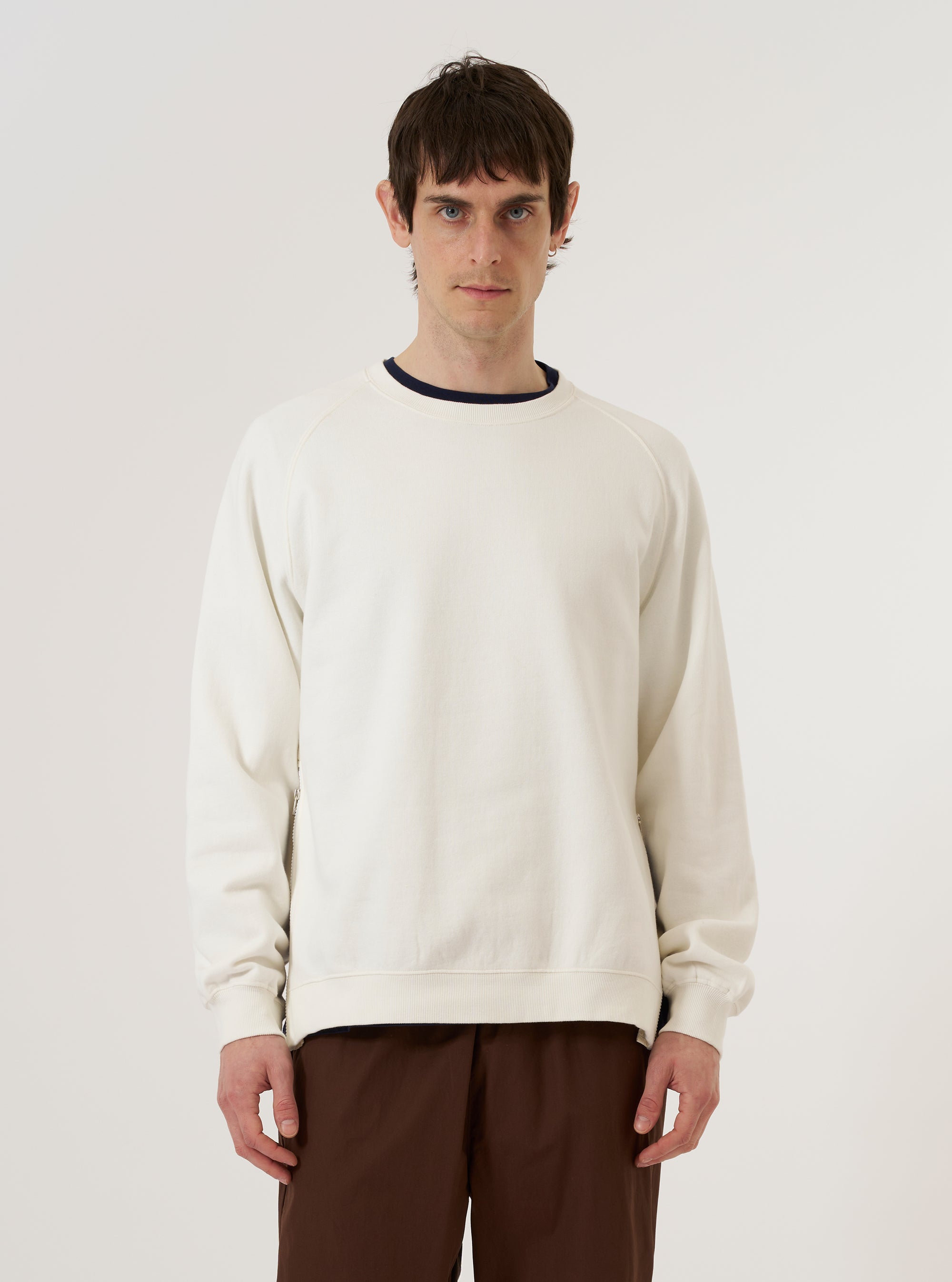 A model wears the Ecru Brush Back Sweat Billy Sweat against a plain, light grey background. The sweatshirt features a relaxed fit, a crew neckline, and ribbed cuffs and hem. The ecru-colored cotton fabric has a soft, matte appearance. The model is shown from the front, highlighting the garment's clean design and classic sweatshirt construction.