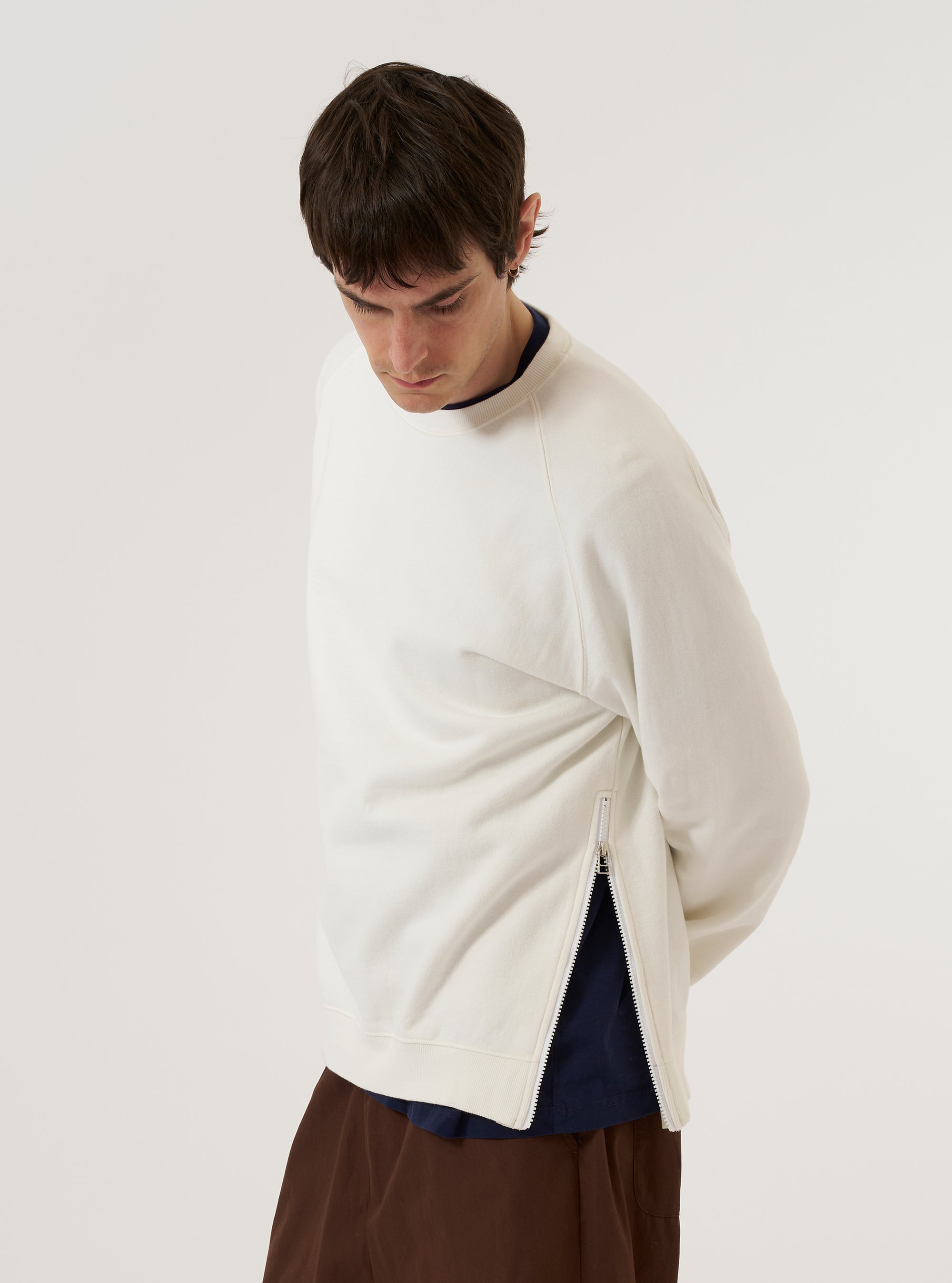 A model wears the Ecru Brush Back Sweat Billy Sweat, shown from a three-quarter rear angle against a plain, neutral background. The sweatshirt features a classic crew neckline, long sleeves with ribbed cuffs, and a ribbed hem. The ecru-colored cotton fabric has a soft, brushed-back appearance and a relaxed silhouette. No mannequin is present in the image.