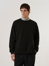 A model wears the Black Brush Back Sweat Billy Sweat against a plain white background. The sweatshirt features a classic crew neckline, long sleeves with ribbed cuffs, and a ribbed hem. The garment is made from a solid black brush-back cotton fabric and has a relaxed fit.