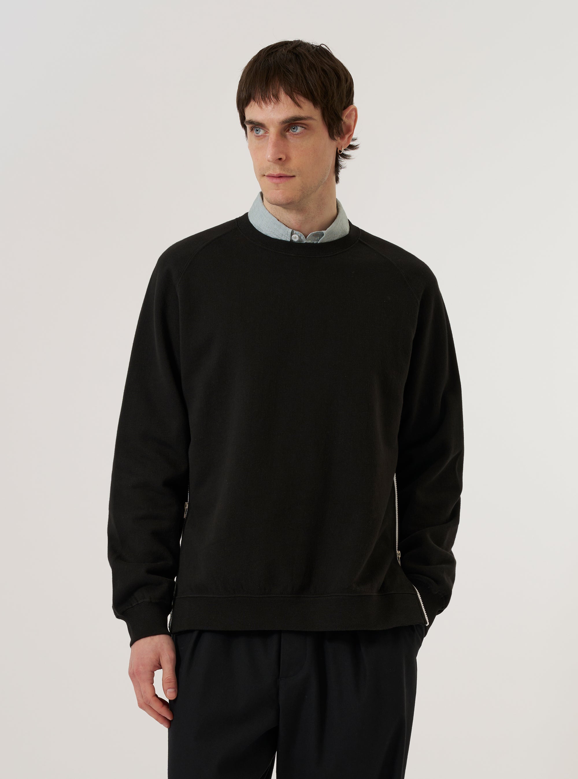 A model wears the Black Brush Back Sweat Billy Sweat against a plain white background. The sweatshirt features a classic crew neckline, long sleeves with ribbed cuffs, and a ribbed hem. The garment is made from a solid black brush-back cotton fabric and has a relaxed fit.