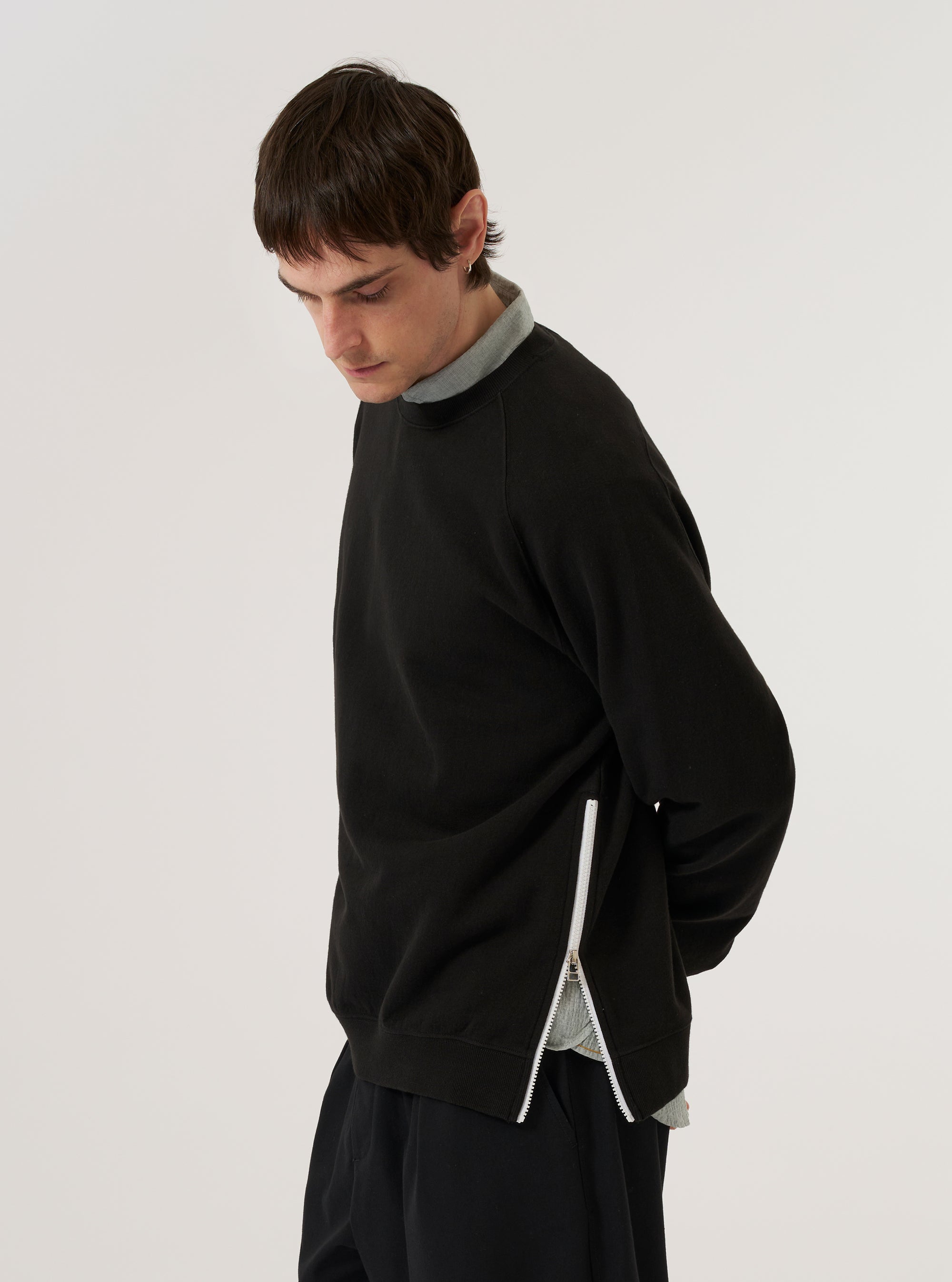 A model wears the Black Brush Back Sweat Billy Sweat, shown from a side profile against a plain white background. The sweatshirt features a crew neckline, ribbed cuffs, and a ribbed hem. The garment is made from a solid black brush-back cotton fabric with a smooth finish.