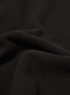 A close-up fabric swatch of the Black Brush Back Sweat Billy Sweat highlights the soft, matte texture of the black cotton material. The image focuses entirely on the fabric's surface, providing a detailed view of its color and composition.