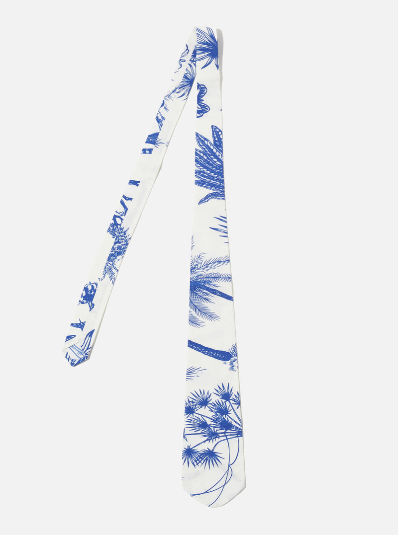 The White Jungle Toile Poplin Tie is presented as a flat lay against a white background. The tie features a vibrant, all-over jungle print with green foliage and animal motifs on a white cotton poplin base. It has a distinctive asymmetric, off-centre design with a pointed tip.