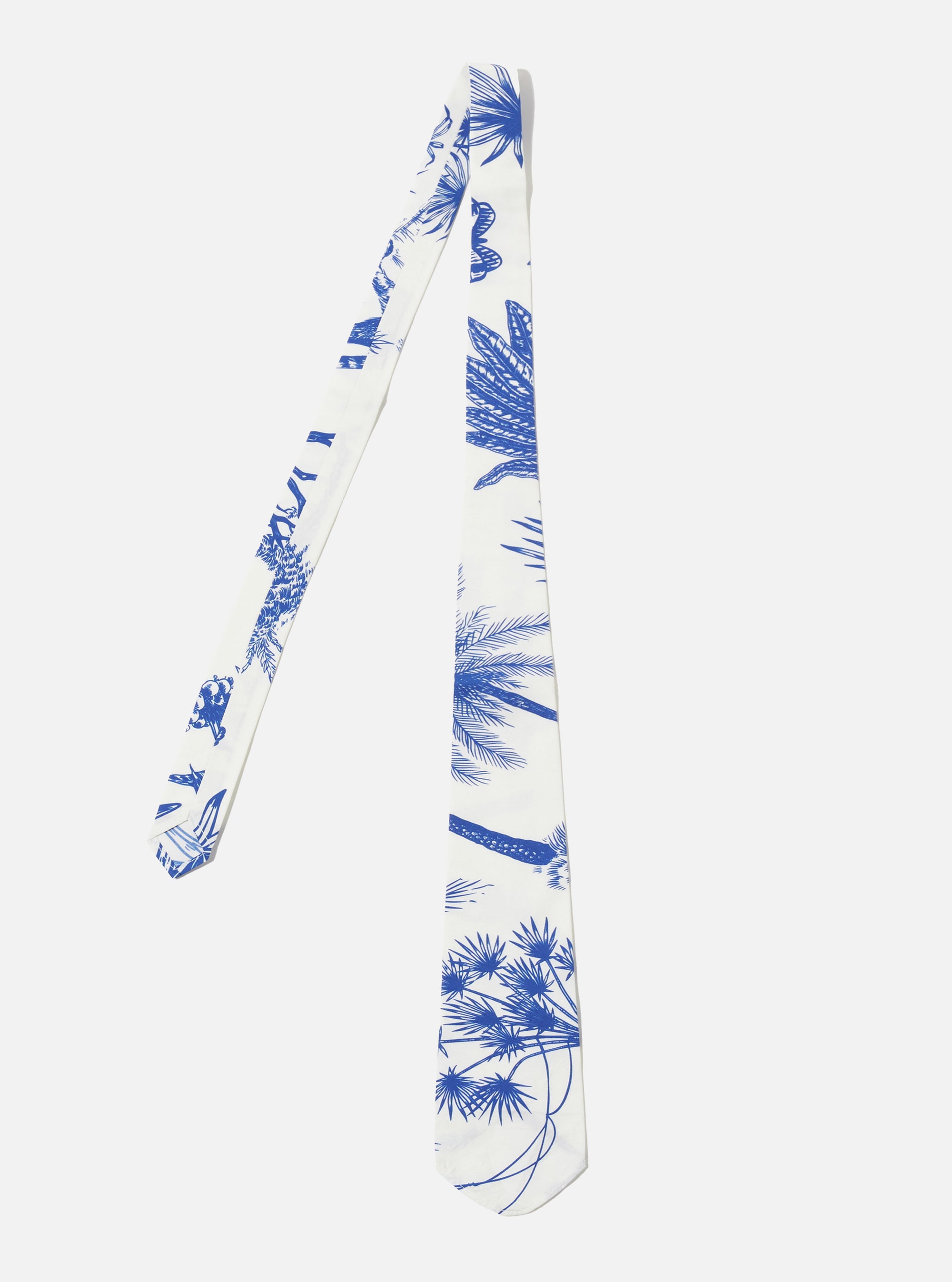 The White Jungle Toile Poplin Tie is presented as a flat lay against a white background. The tie features a vibrant, all-over jungle print with green foliage and animal motifs on a white cotton poplin base. It has a distinctive asymmetric, off-centre design with a pointed tip.