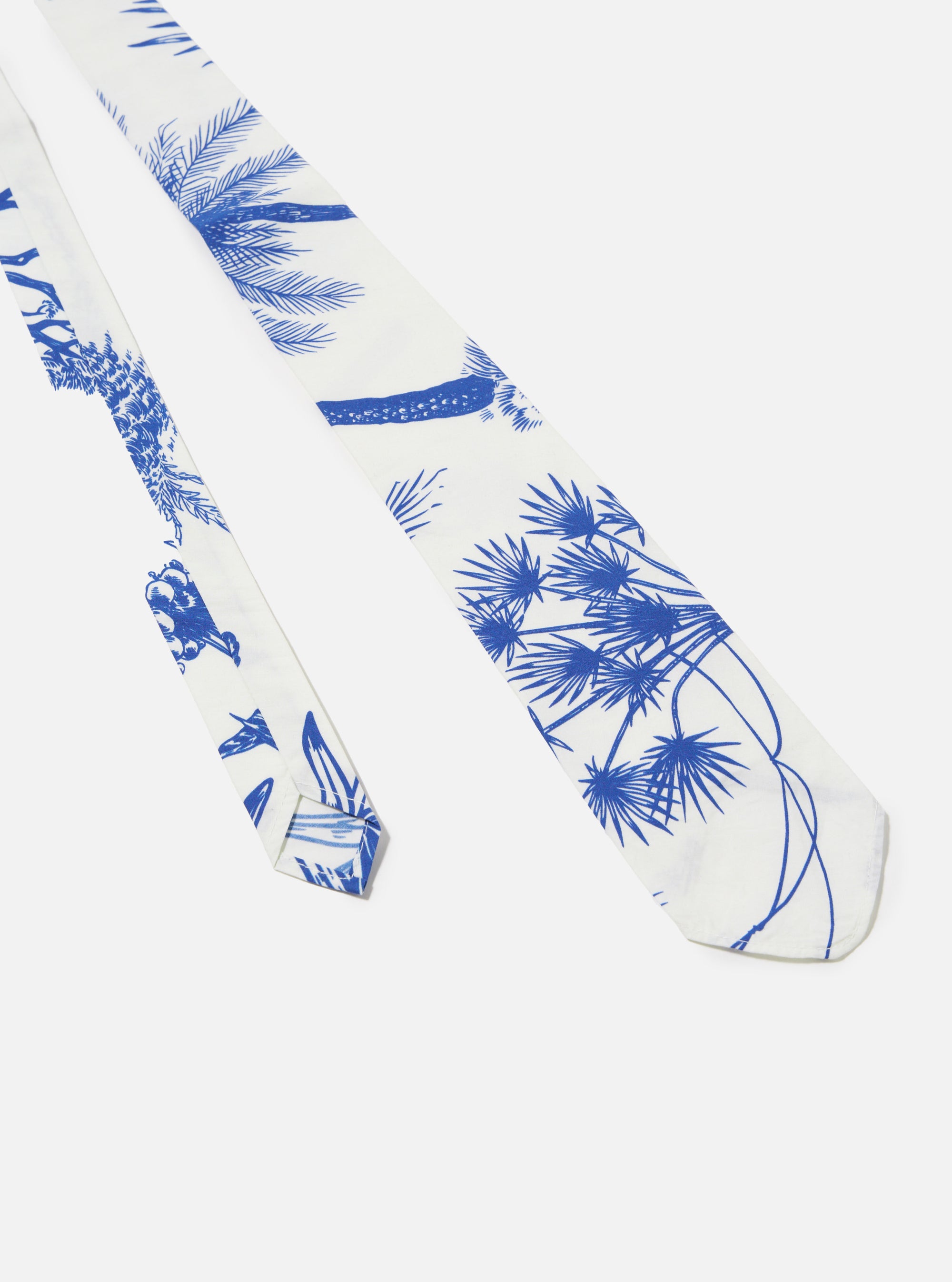 The White Jungle Toile Poplin Tie is shown from a rear angle as a flat lay against a white background. This view highlights the reverse side of the tie, showing the construction, the keeper loop, and the intricate green and blue jungle-themed toile print against the ecru fabric.