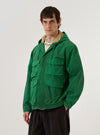 A model wears the Green Recycled Splash Nylon Longsands Jacket against a plain white background. The jacket features an integrated hood, a concealed front closure, and four prominent 3D flap pockets on the front. The garment is made from a lightweight green recycled nylon with a smooth, technical finish.