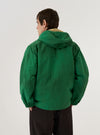 A model wears the Green Recycled Splash Nylon Longsands Jacket against a plain white background. The image shows the back of the garment, highlighting the integrated hood, long sleeves, and the smooth, lightweight texture of the green recycled nylon fabric. The jacket features a relaxed fit with a straight hem. No mannequin is present in the image.