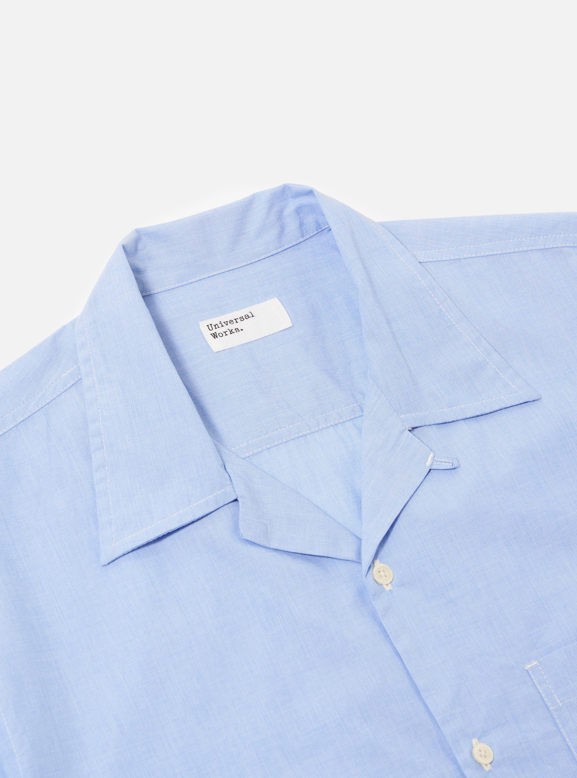 The Sky Fil A Fil Camp Shirt is shown in a detail view as a flat lay against a plain white background. The image focuses on the upper portion of the shirt, highlighting the unstructured camp collar, the button-down front, and the light blue end-on-end weave of the cotton fabric.