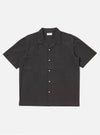 The Black Tech Cotton S/S Dwight Overshirt is shown as a flat lay against a white background. The short-sleeved overshirt features a straight hem, a button-down front with a camp collar, and four front patch pockets. Two rows of vertical sewn pleats run down the front on either side of the buttons. The fabric is a smooth black tech cotton.