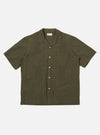 The Olive Tech Cotton S/S Dwight Overshirt is shown as a flat lay against a white background. The short-sleeved overshirt features a camp collar, a six-button front closure, and four front patch pockets. Two rows of vertical pleats are sewn down the front on either side of the buttons. The garment is made from a smooth olive green cotton fabric with a straight hem.