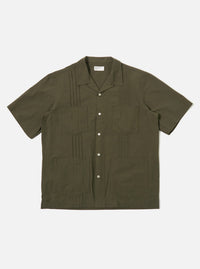 The Olive Tech Cotton S/S Dwight Overshirt is shown as a flat lay against a white background. The short-sleeved overshirt features a camp collar, a six-button front closure, and four front patch pockets. Two rows of vertical pleats are sewn down the front on either side of the buttons. The garment is made from a smooth olive green cotton fabric with a straight hem.
