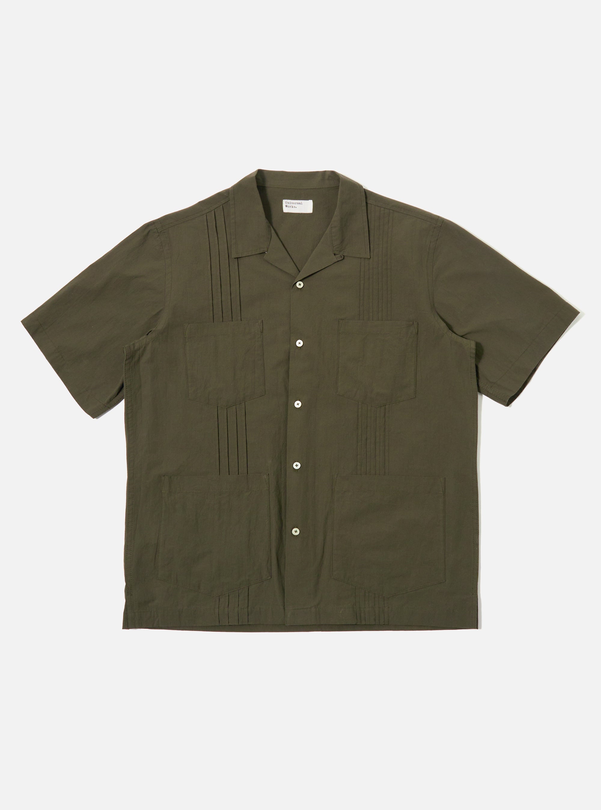 The Olive Tech Cotton S/S Dwight Overshirt is shown as a flat lay against a white background. The short-sleeved overshirt features a camp collar, a six-button front closure, and four front patch pockets. Two rows of vertical pleats are sewn down the front on either side of the buttons. The garment is made from a smooth olive green cotton fabric with a straight hem.