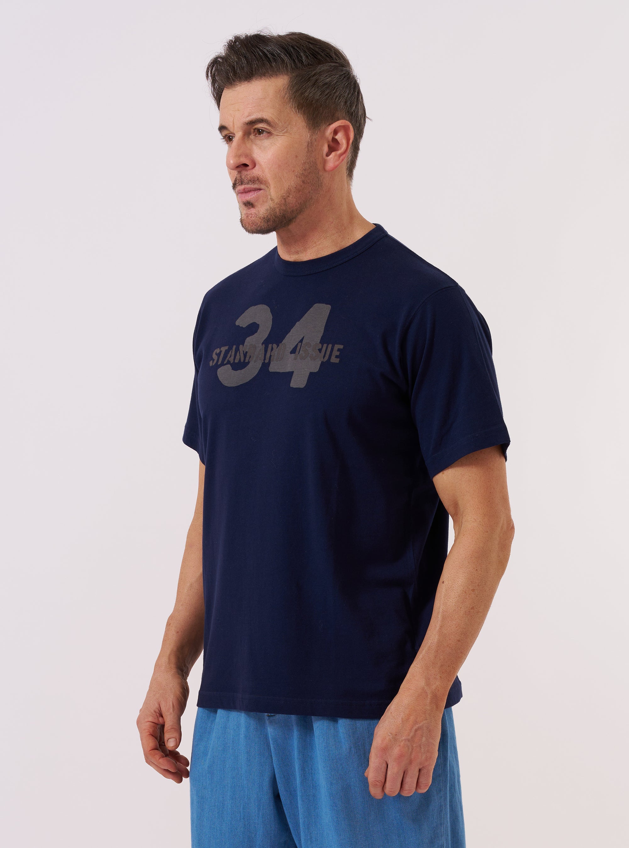 A model wears the Navy Single Jersey 34 Printed Core Tee against a plain white background. The short-sleeve t-shirt features a classic crew neckline and a prominent graphic print on the chest. The garment is constructed from a dark navy single jersey cotton fabric.